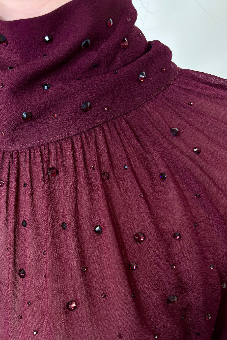 Close-up of woman wearing a burgundy mesh long sleeve top with crystal embellishments 