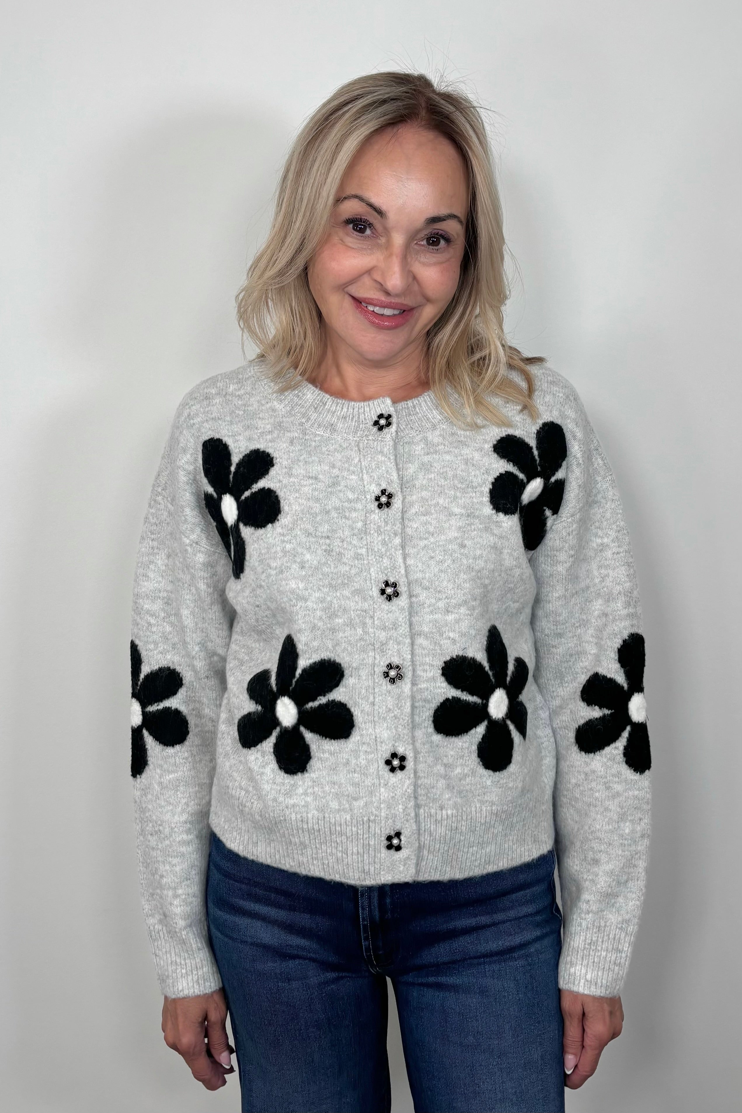 Front view of woman wearing a gray cardigan with a black daisy pattern and buttons, done up