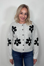 Front view of woman wearing a gray cardigan with a black daisy pattern and buttons, done up