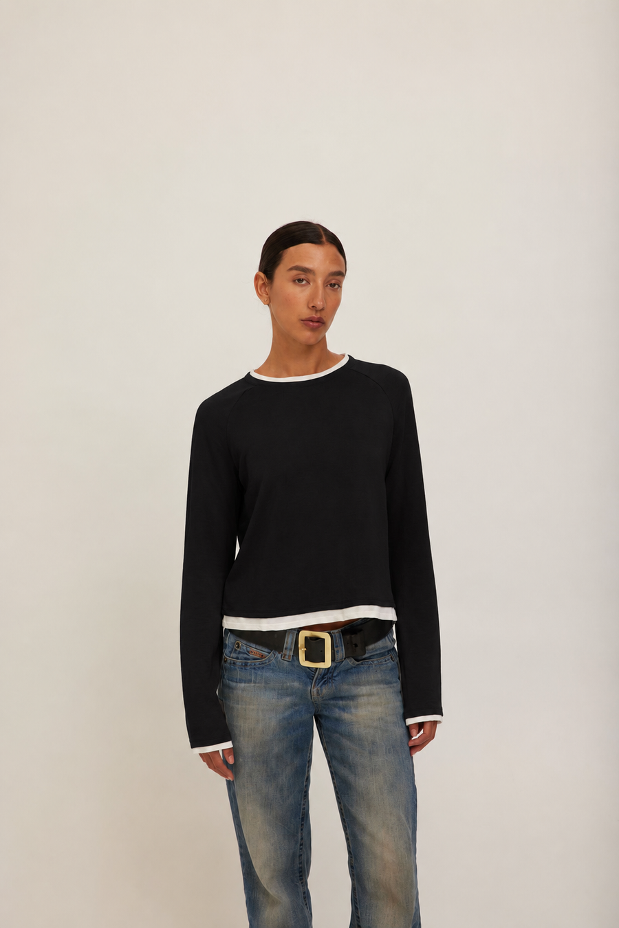 A model wearing a black long-sleeve crewneck sweater with white ribbed trim at the collar, cuffs, and hem. 