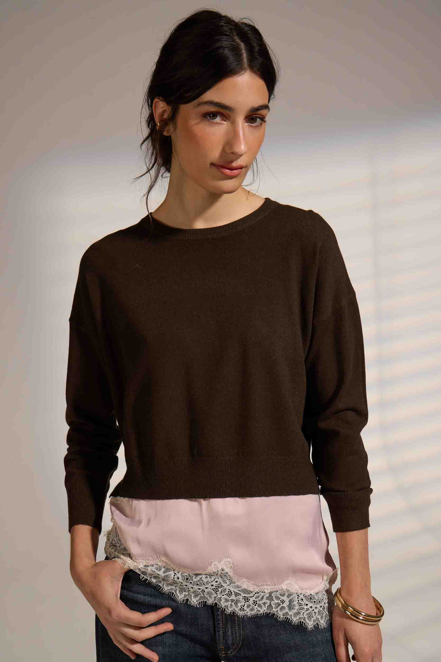 A woman modeling a dark brown crewneck sweater with a layered look,