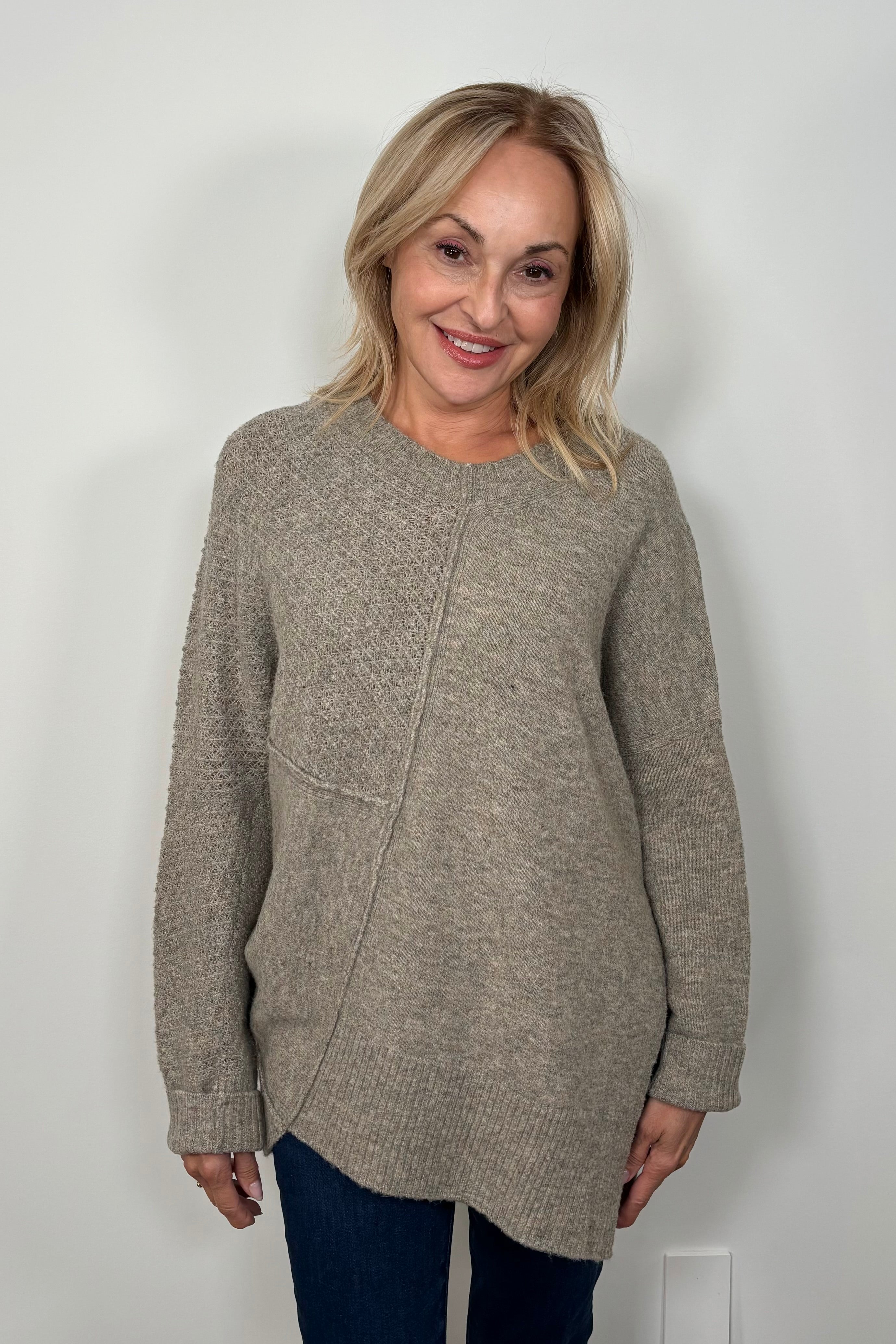 Front view of woman wearing a greige asymmetrical sweater 