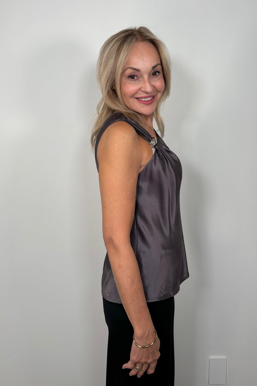 Side view of woman wearing a deep metallic gray satin tank top with a silver metal detail