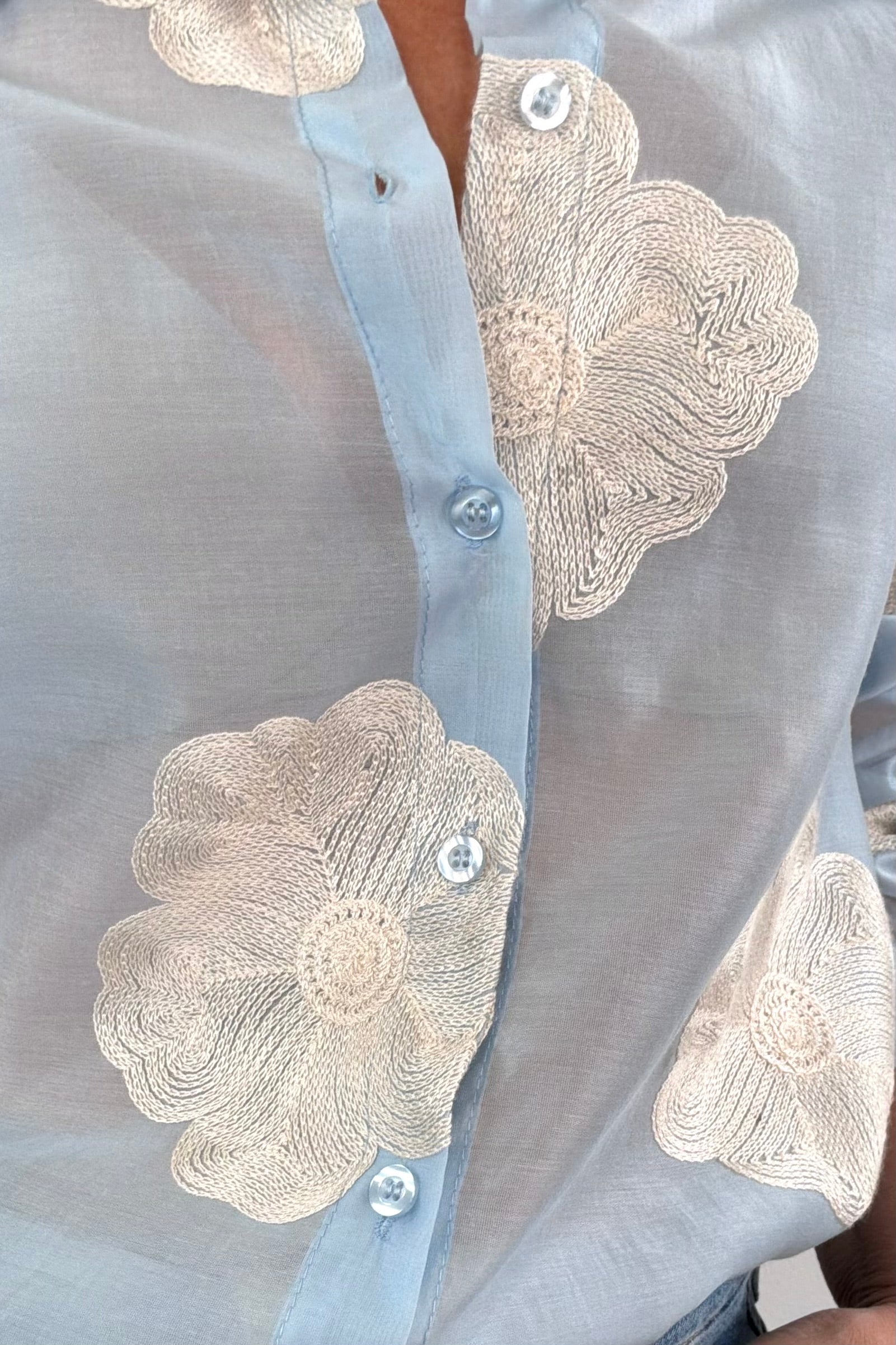 Close up of Woman wearing a light blue button up blouse with white floral detail