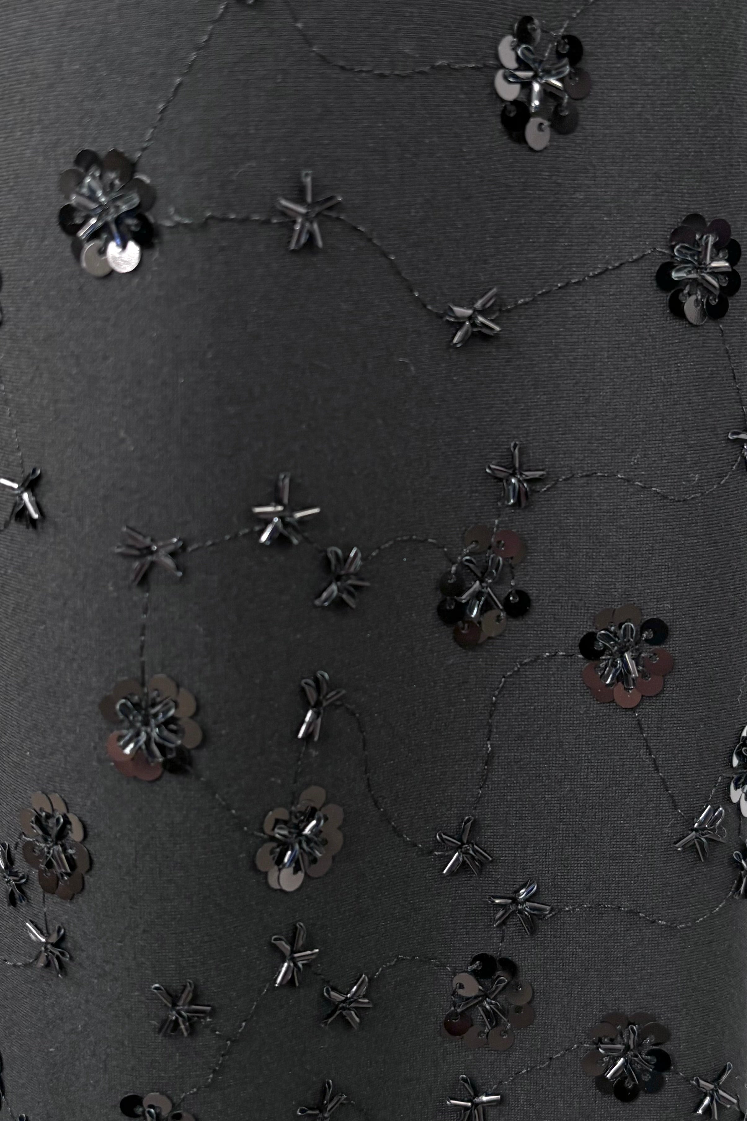 Black fabric with floral embellishments and sequins on a textured background