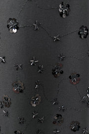 Black fabric with floral embellishments and sequins on a textured background