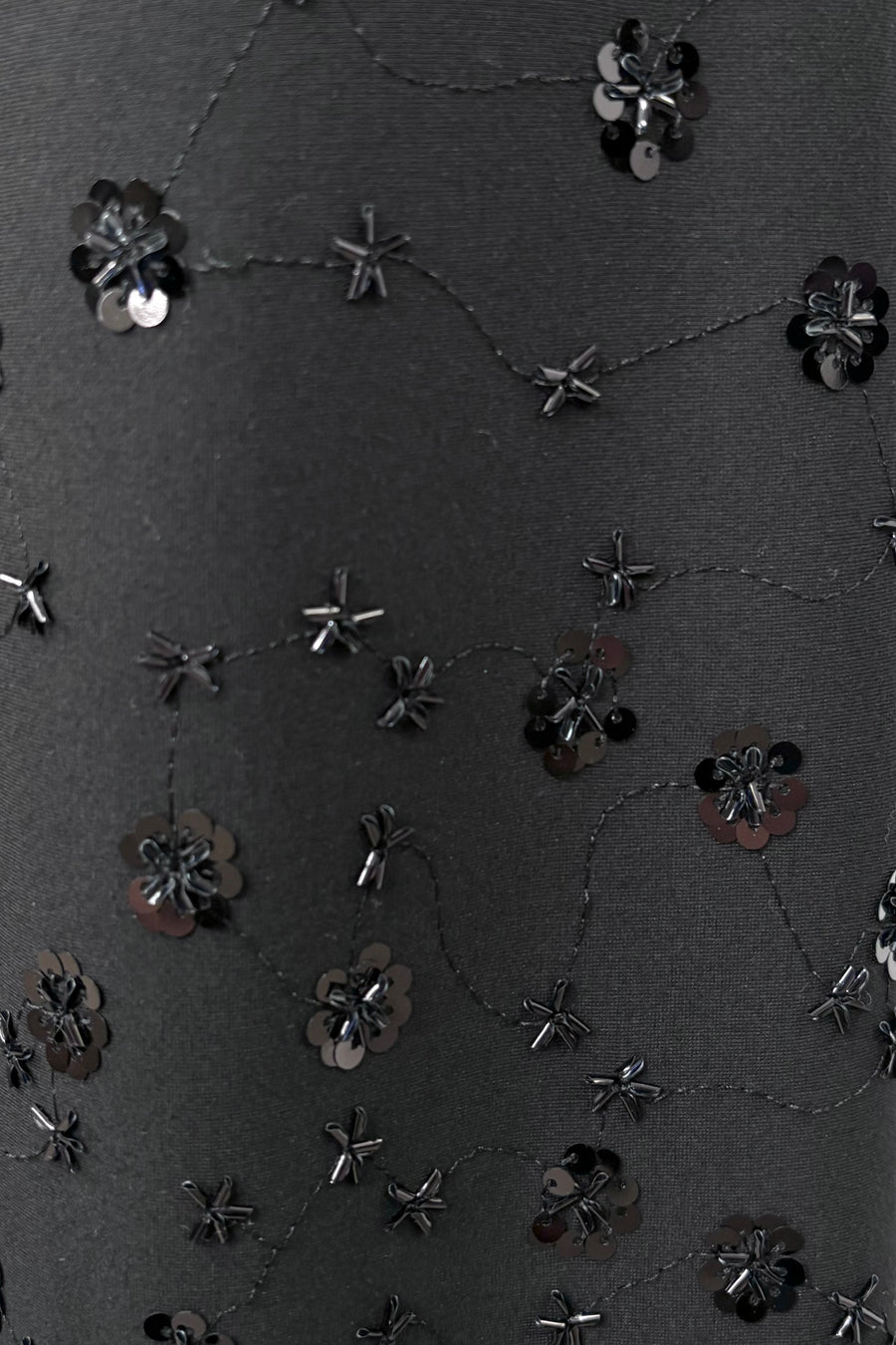 Black fabric with floral embellishments and sequins on a textured background