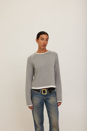 A model wearing a grey long-sleeve crewneck sweater with white ribbed trim at the collar, cuffs, and hem. 