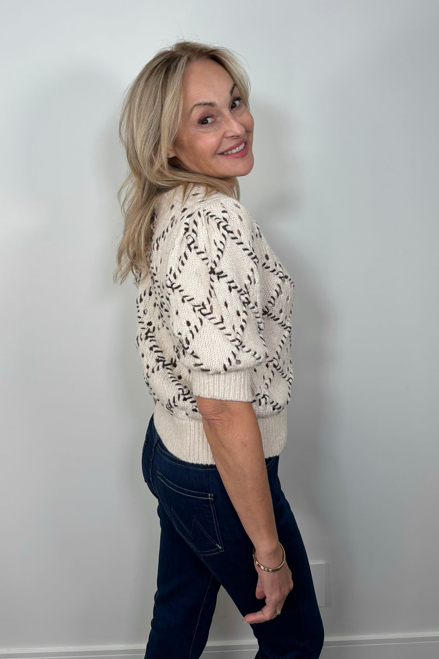 Side view of a woman wearing a white knit cardigan with whipstitch detailing 