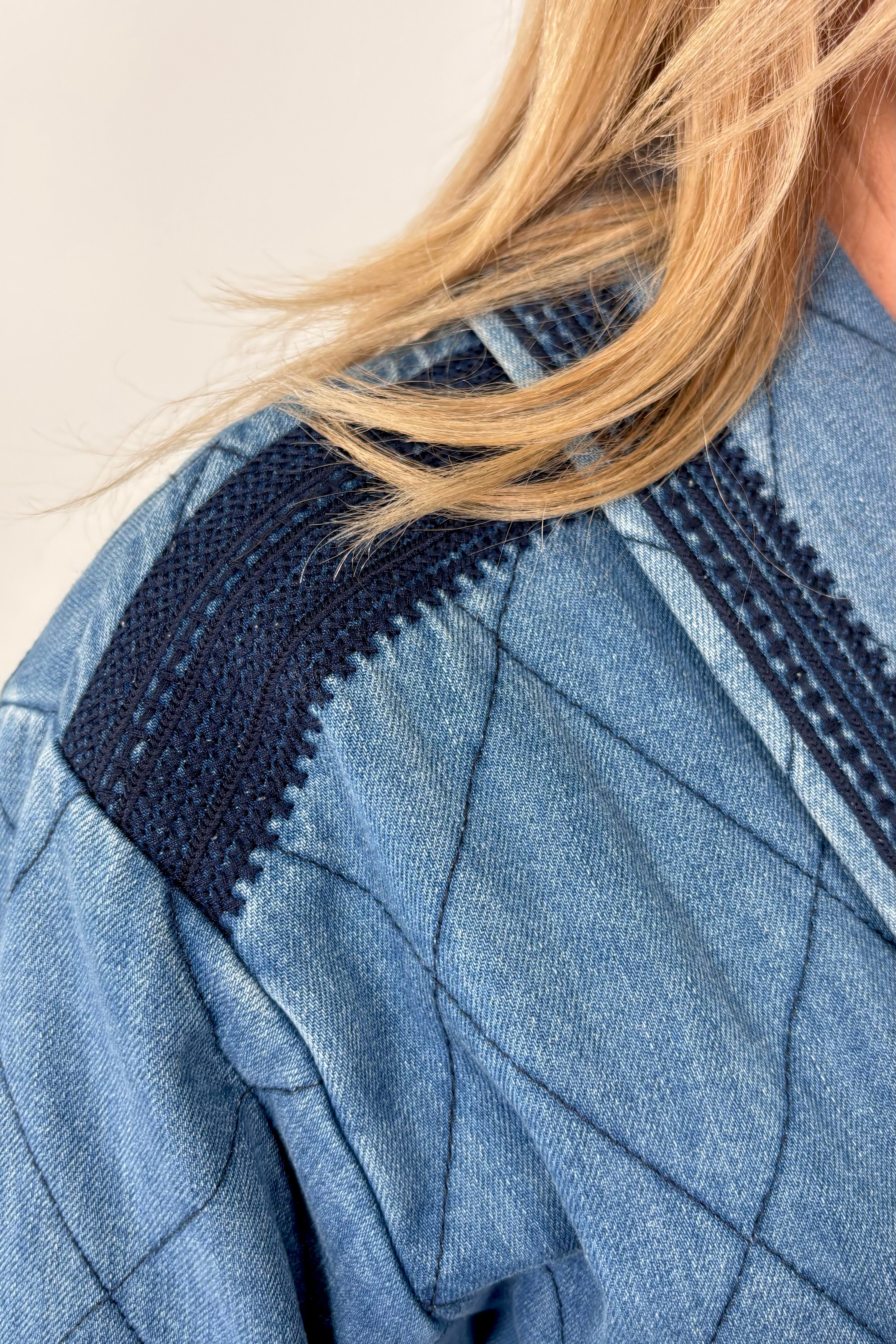 Zoom into woman’s shoulder wearing a blue quilted jacket with navy blue detailing.