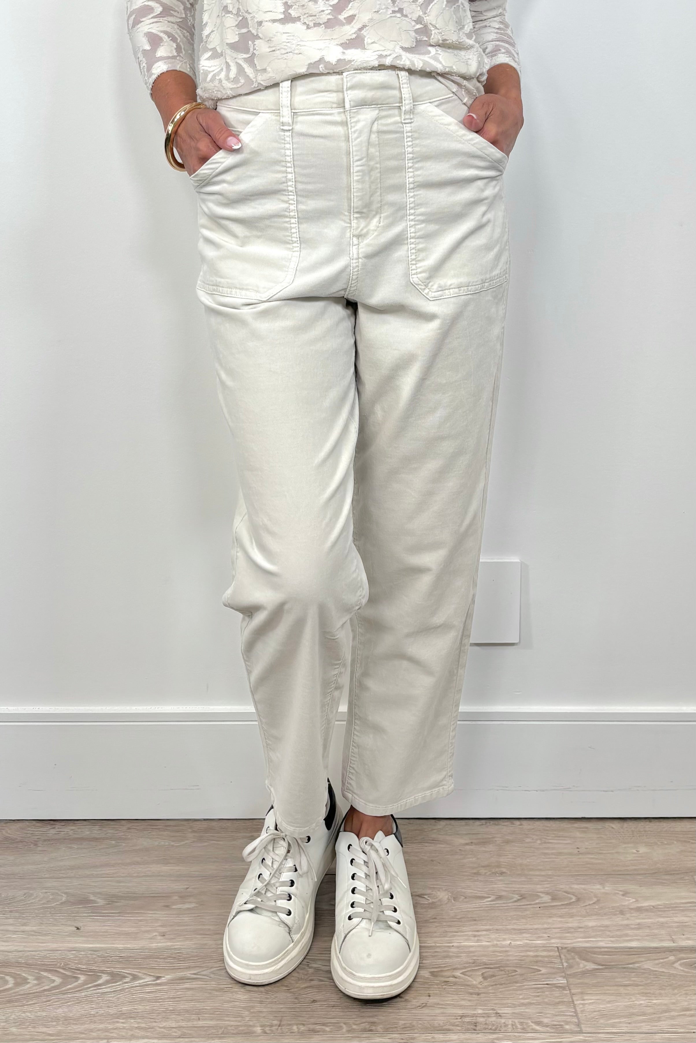 Front view of a person wearing oat-coloured corduroy pants and white sneakers on a plain background