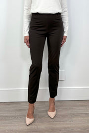 Person wearing dark brown fitted pants with nude heels against a white wall.