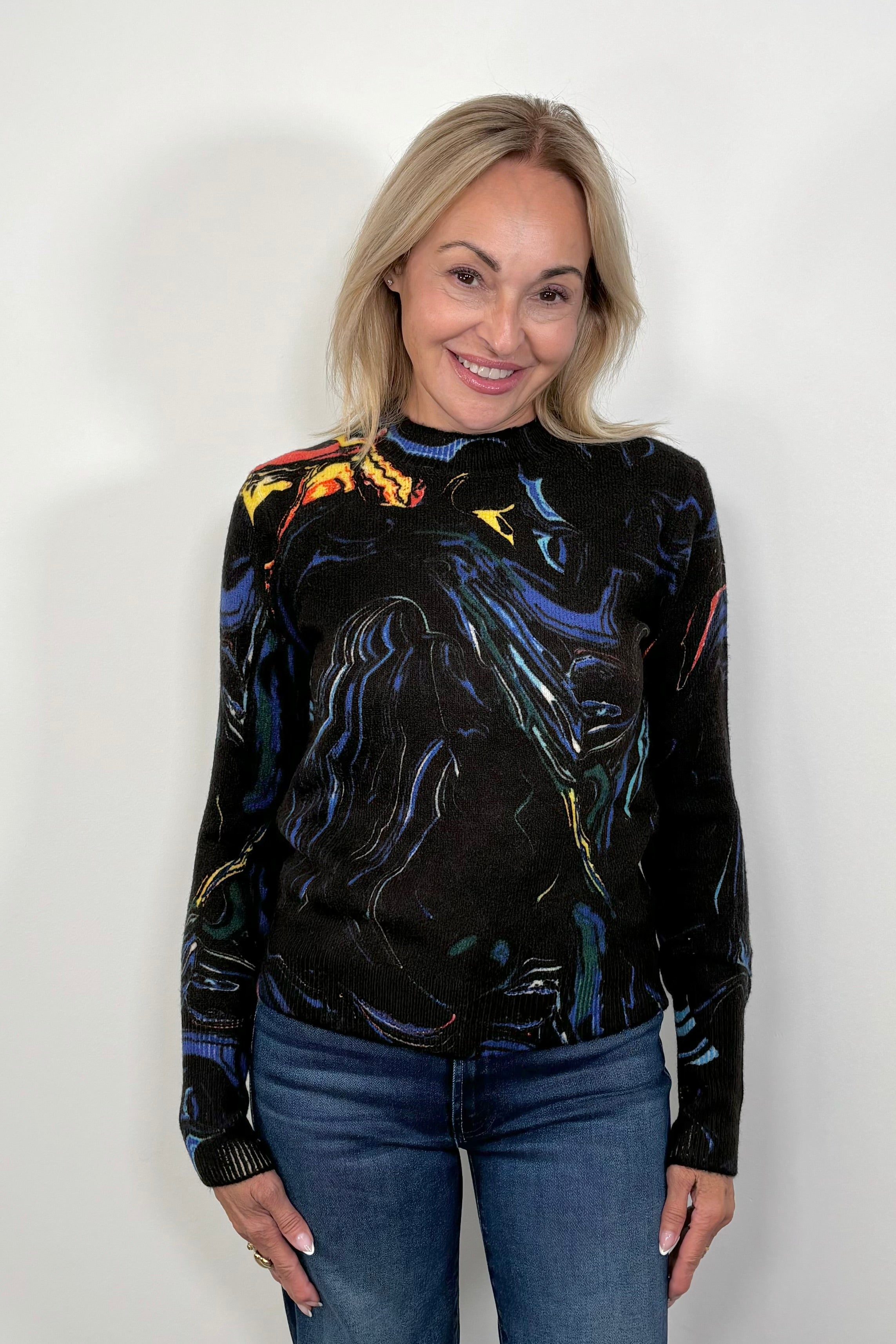 Woman wearing a black long-sleeve sweater with colorful abstract design against a white background