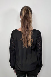 back of a woman wearing a black long sleeve satin blouse with lace detailing on the shoulders