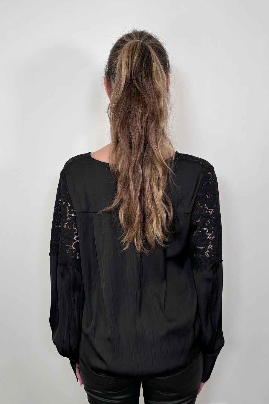 back of a woman wearing a black long sleeve satin blouse with lace detailing on the shoulders
