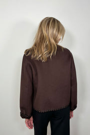 back view of woman wearing a buttoned up brown wool coat with whipstitch detailing