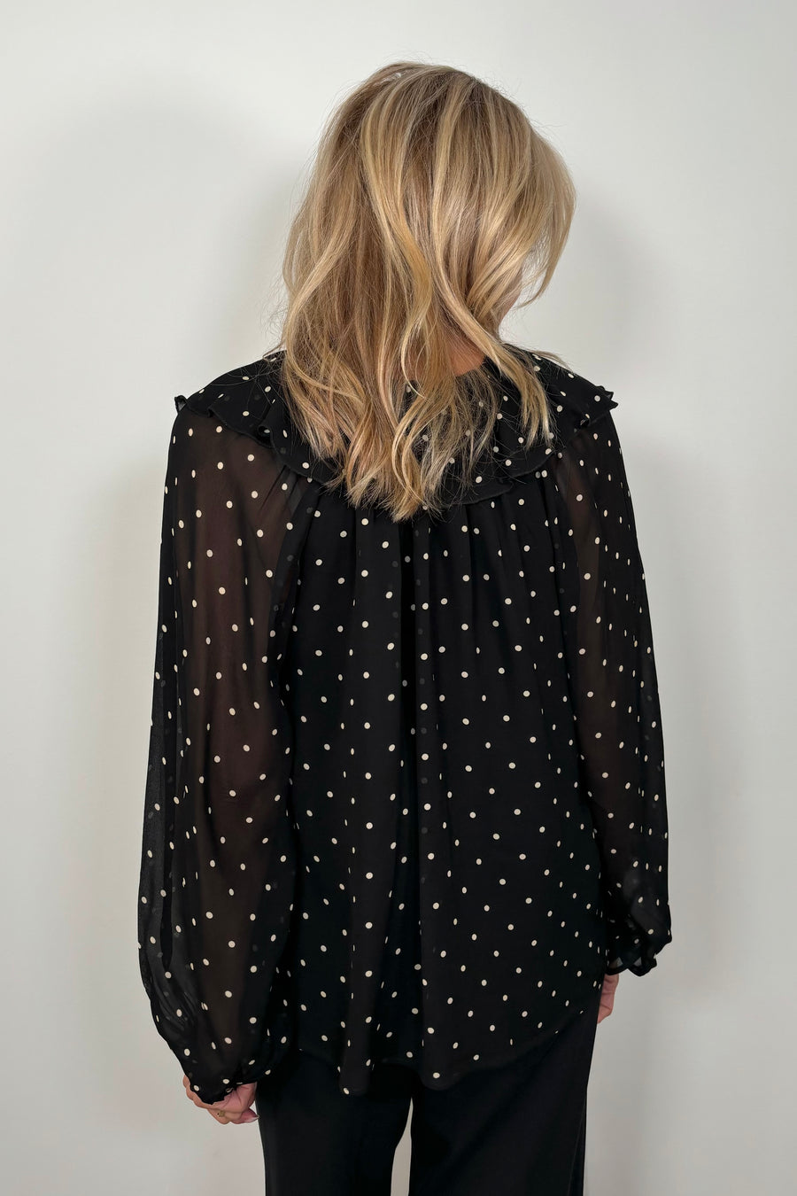 Back view of a woman wearing a sheer polka dot blouse