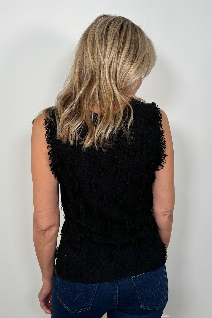 Back view of a woman wearing a black tank top with fine gauge fringes 