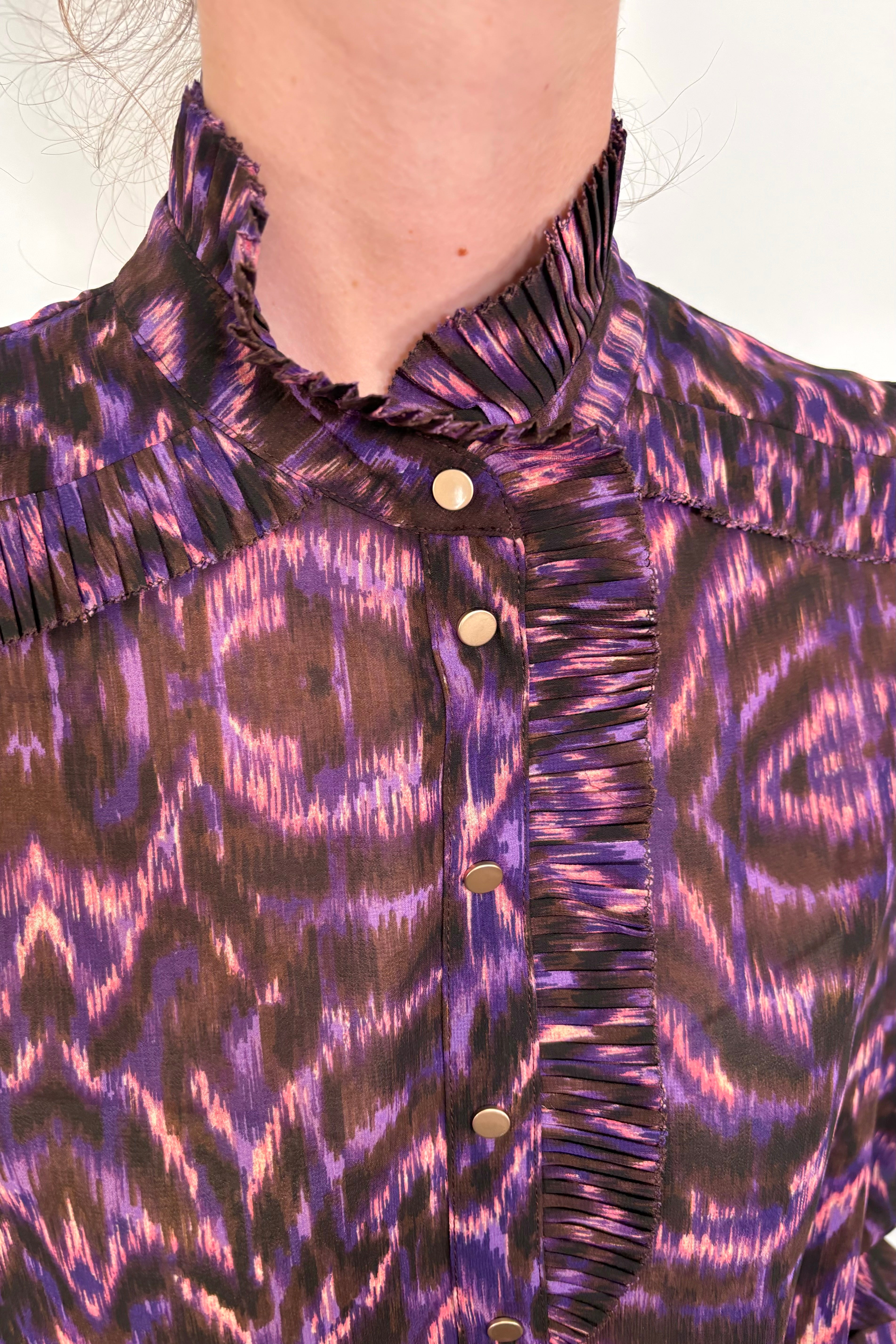 Close up pf the neck of a woman wearing a violet sheer printed blouse with ruffles tucked in