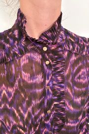 Close up pf the neck of a woman wearing a violet sheer printed blouse with ruffles tucked in