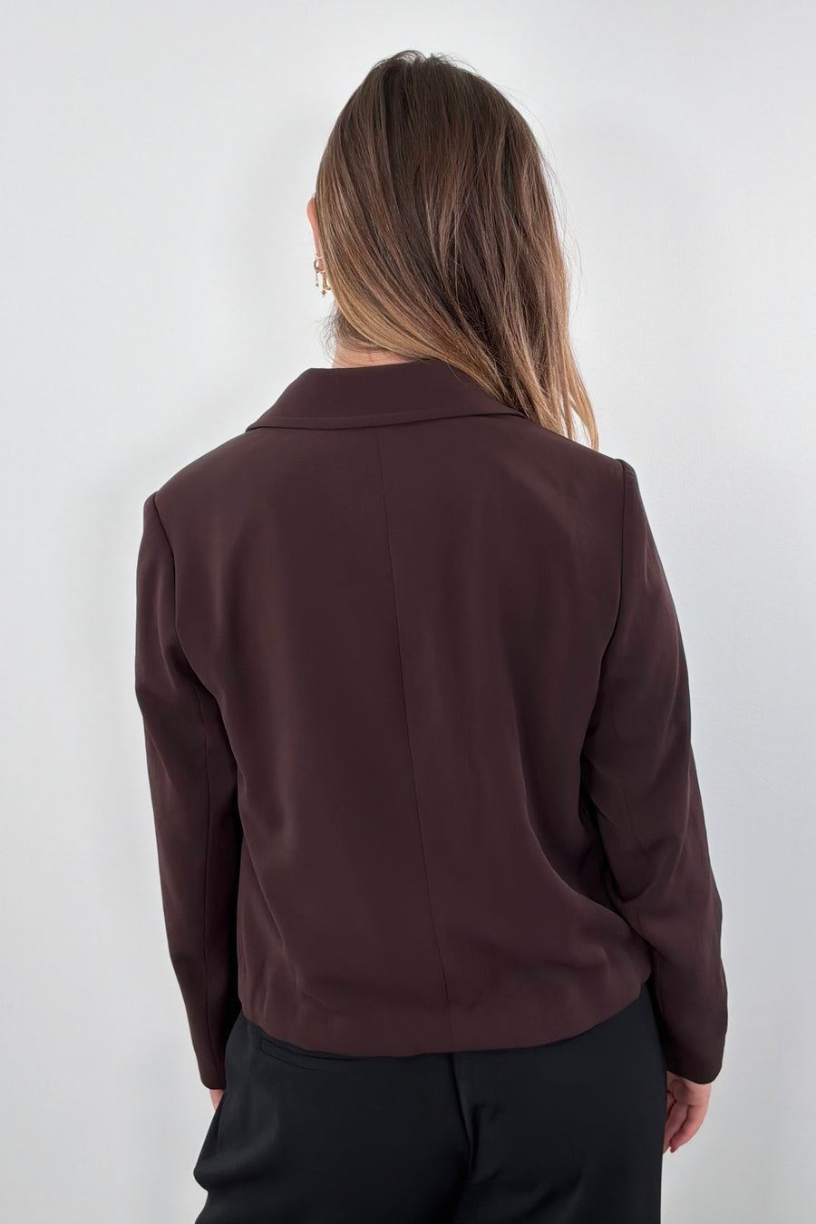 Woman wearing a brown blazer with tie detail at bottom 