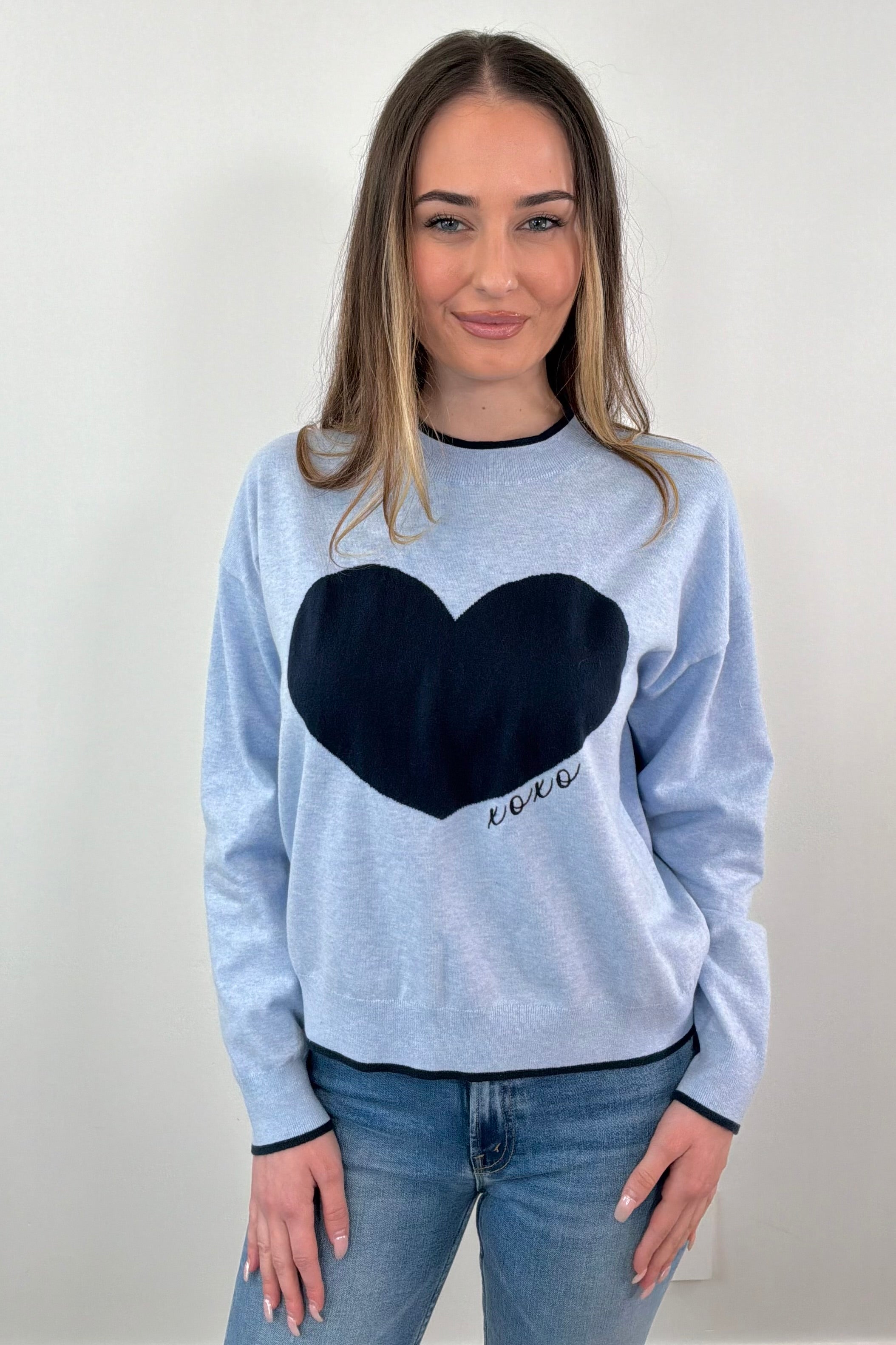 woman wearing a light blue sweater with a navy heart design and "XOXO" embroidered 