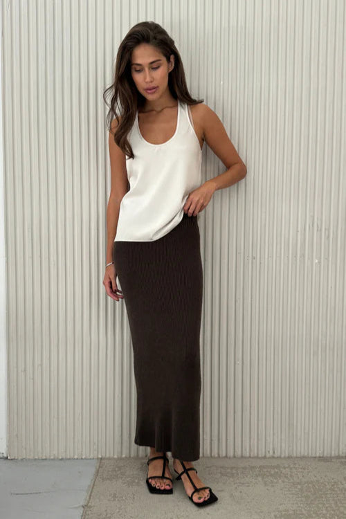 Woman wearing a white top and black skirt against a light-colored wall.