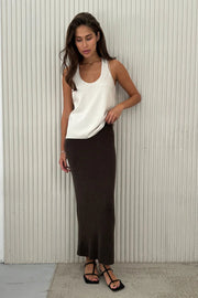 Woman wearing a white top and black skirt against a light-colored wall.