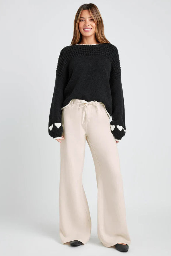 Woman wearing a black sweater with heart details and beige pants on a white background