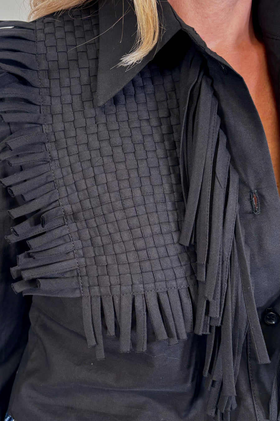 Close-up of a woman wearing a black long sleeve collared blouse with fringes 