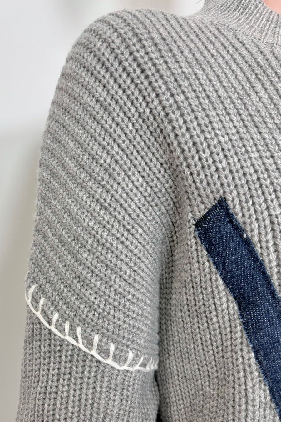 Close up of the shoulder of a gray sweater with whipstitch detailing