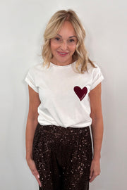 Woman wearing a white t-shirt with a red heart design on a plain background