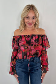 Woman wearing a red and black floral boat-neck top with blue jeans against a plain background