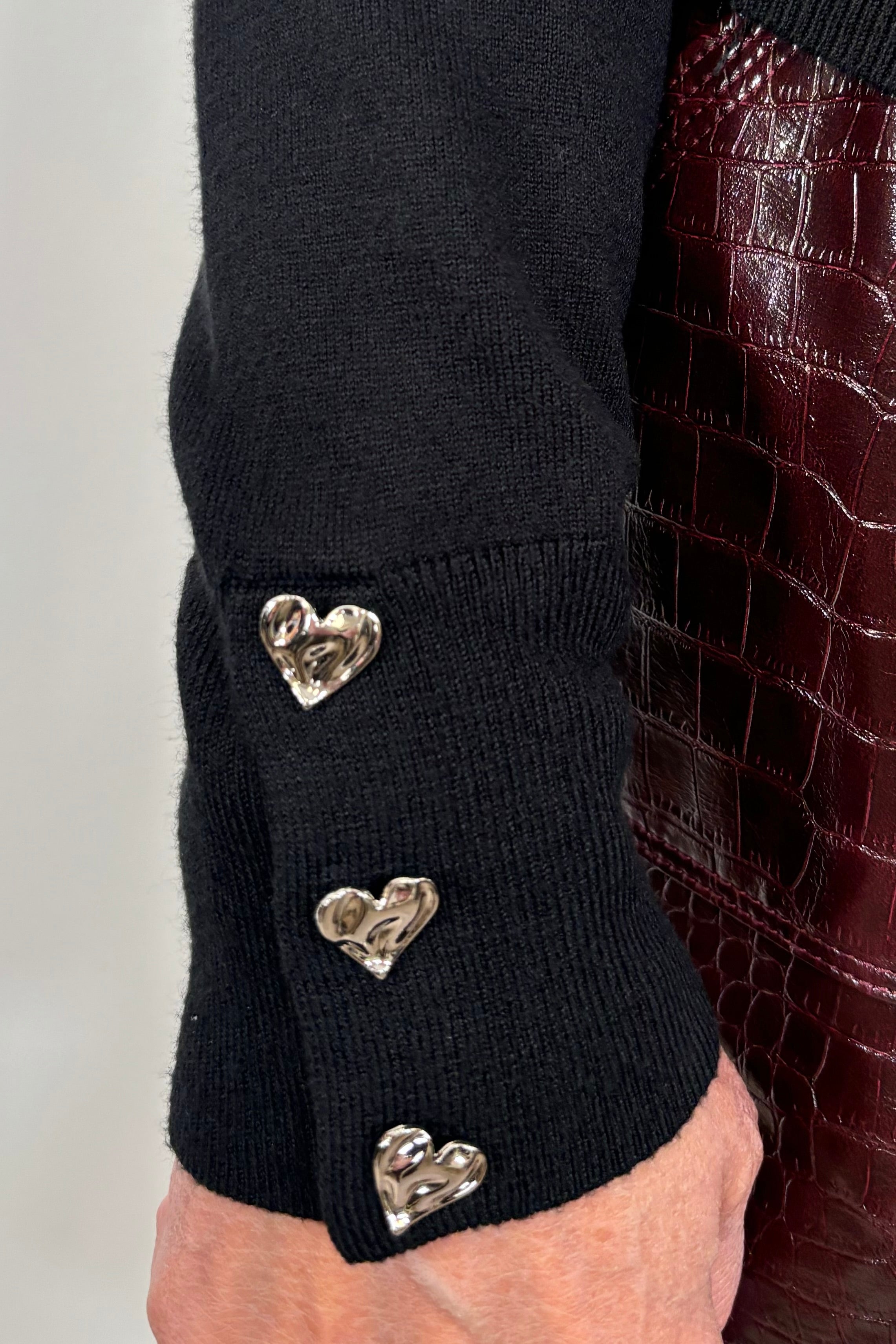Black sweater with silver heart buttons worn by a person.