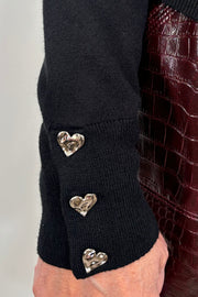 Black sweater with silver heart buttons worn by a person.