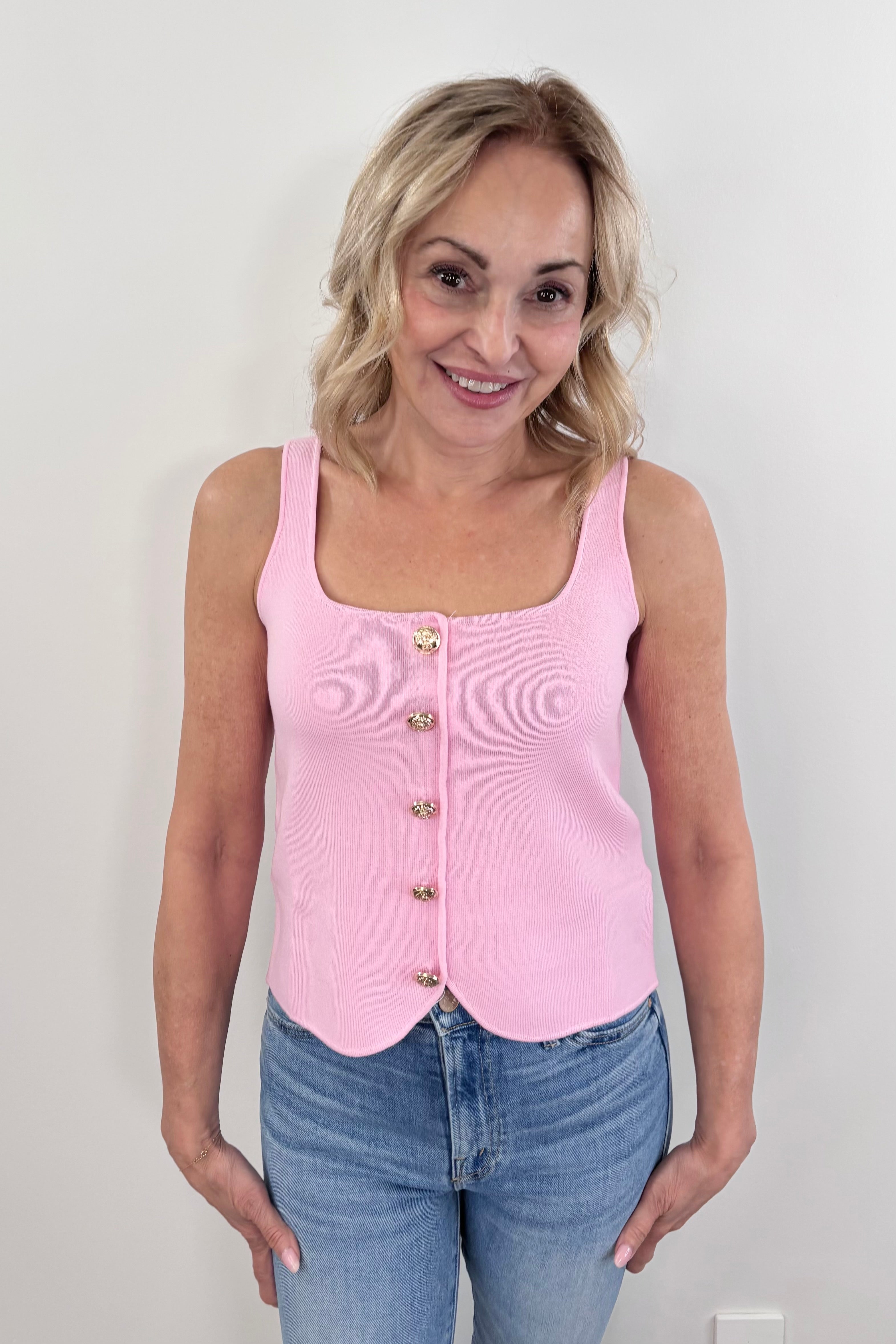 Woman wearing a pink sleeveless knit tank top with front buttons and a scalloped hem, front view