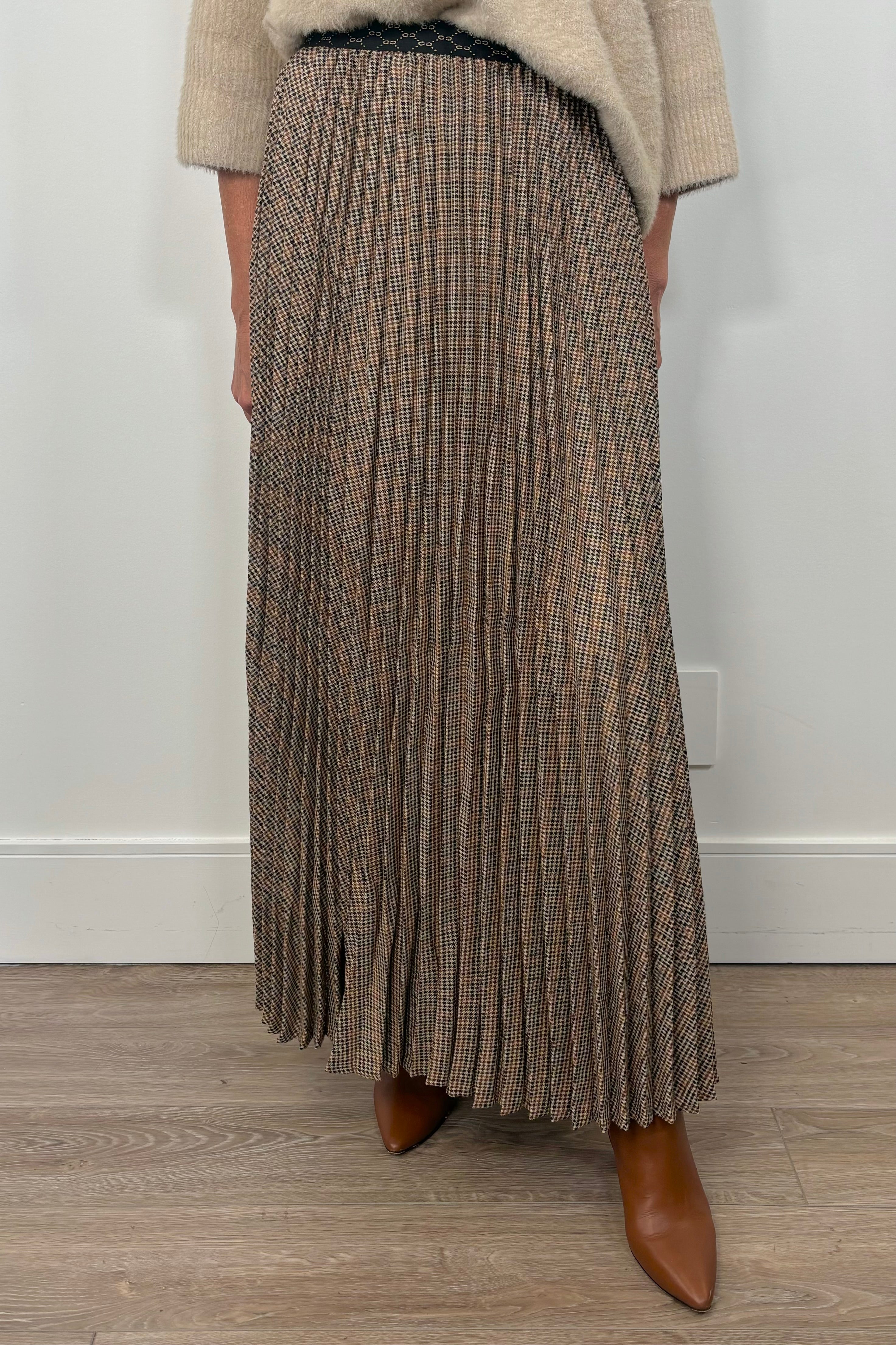Person wearing a long pleated skirt with a neutral background
