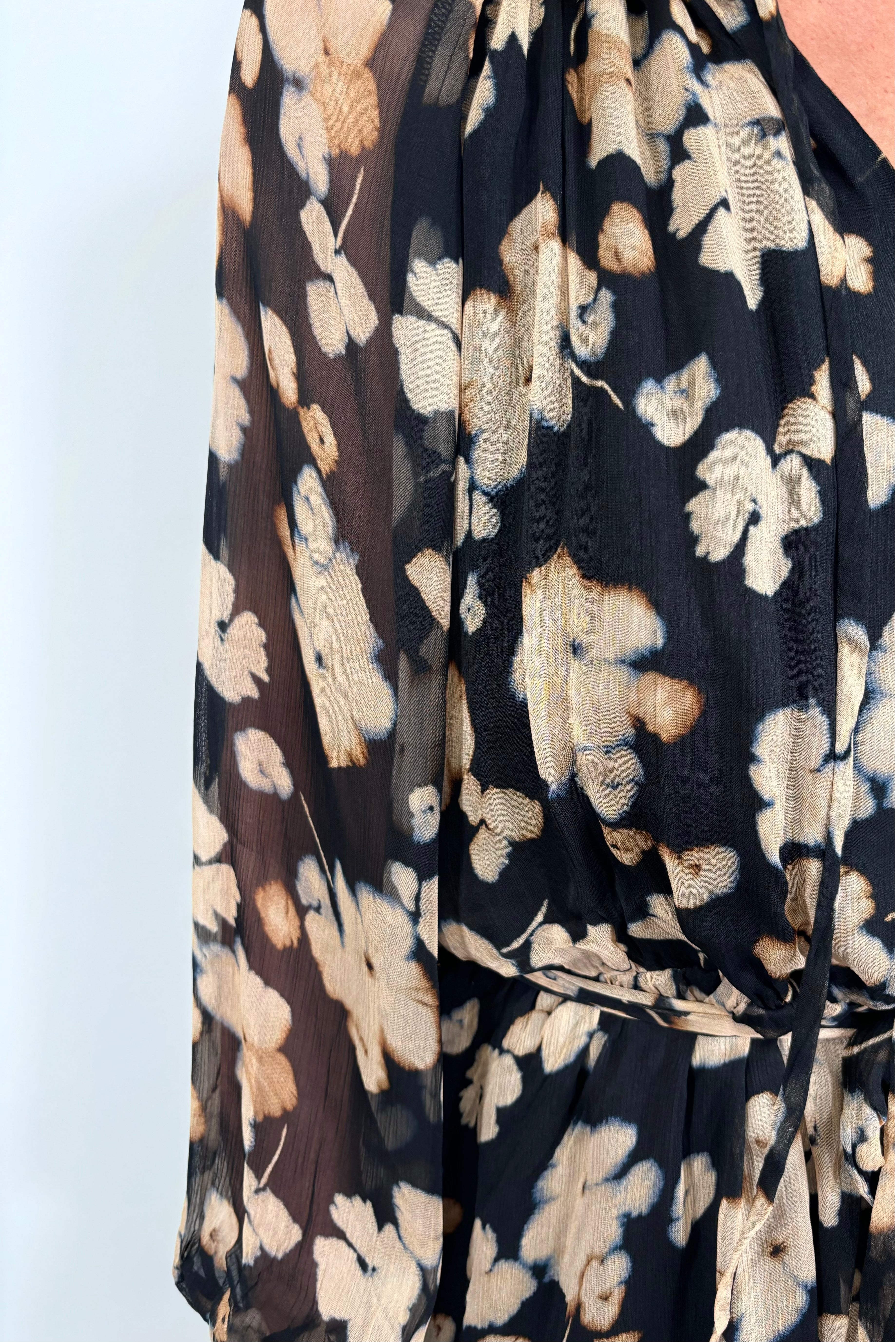close-up of a woman wearing a mini black with beige flowers dress with long sleeves