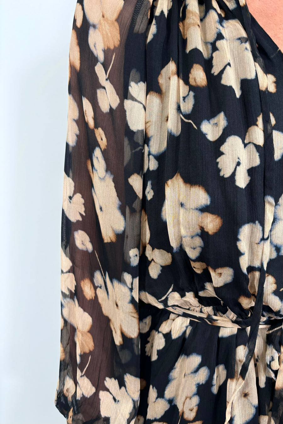 close-up of a woman wearing a mini black with beige flowers dress with long sleeves