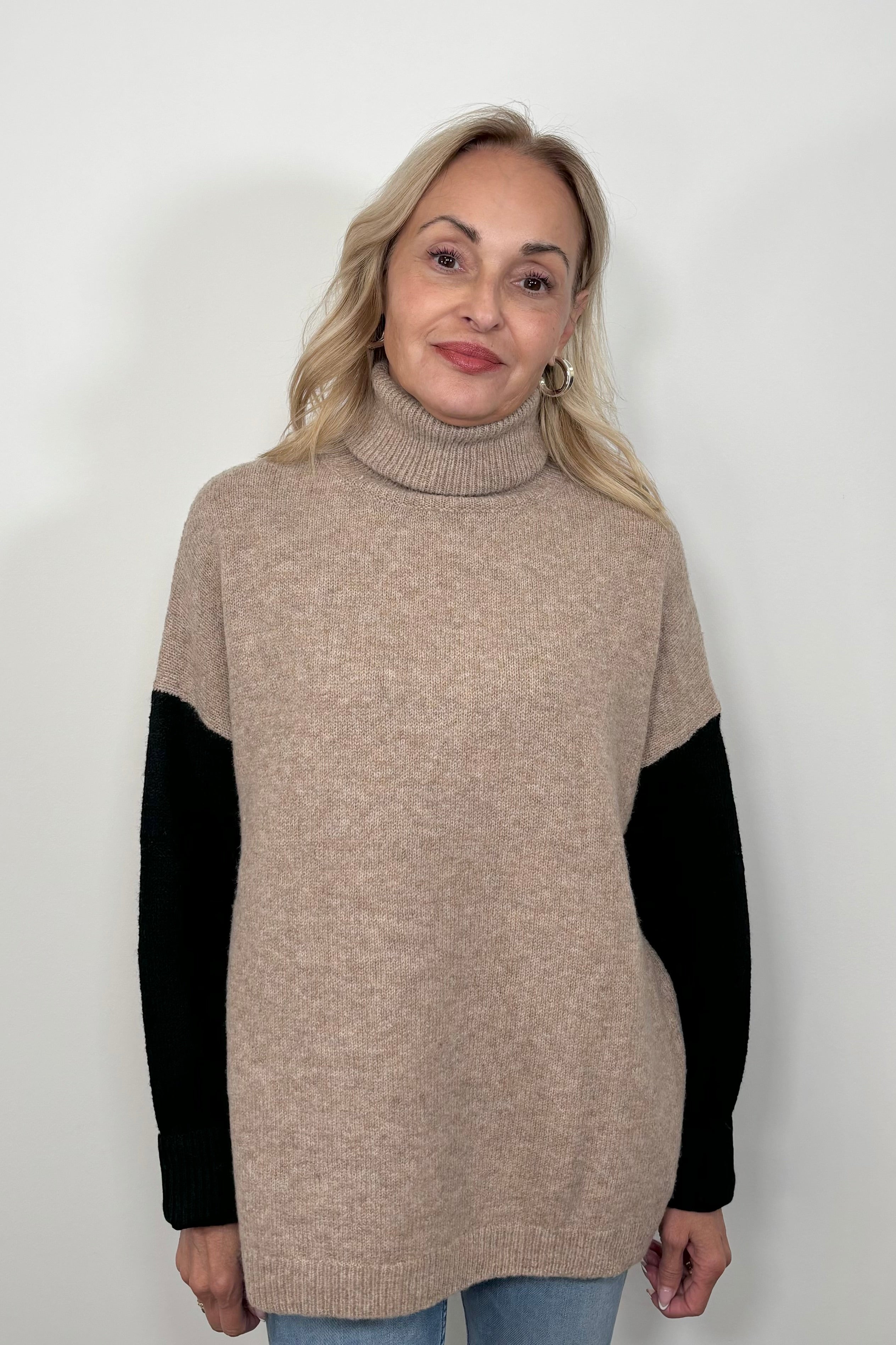 Front view of woman wearing a beige turtle neck sweater with black sleeves and oat meal coloured back