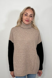 Front view of woman wearing a beige turtle neck sweater with black sleeves and oat meal coloured back