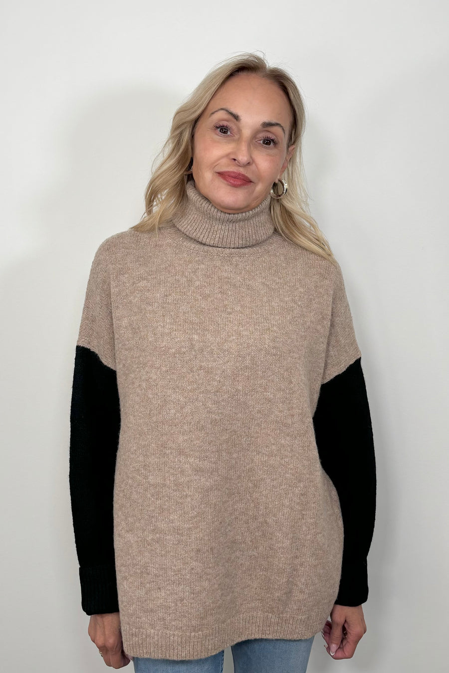 Front view of woman wearing a beige turtle neck sweater with black sleeves and oat meal coloured back