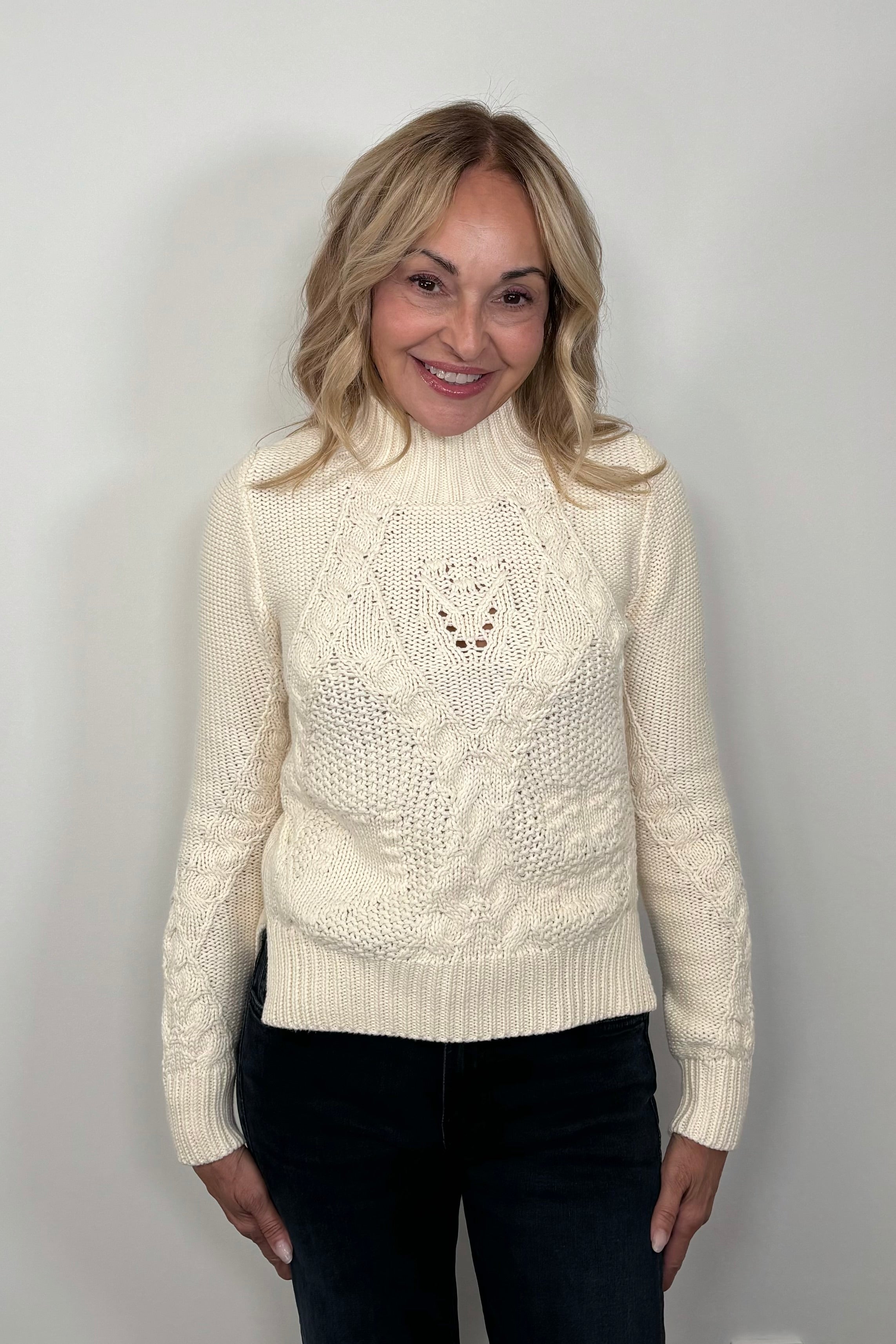 Front view of a woman wearing a cream-colored cable knit sweater 