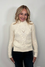 Front view of a woman wearing a cream-colored cable knit sweater 