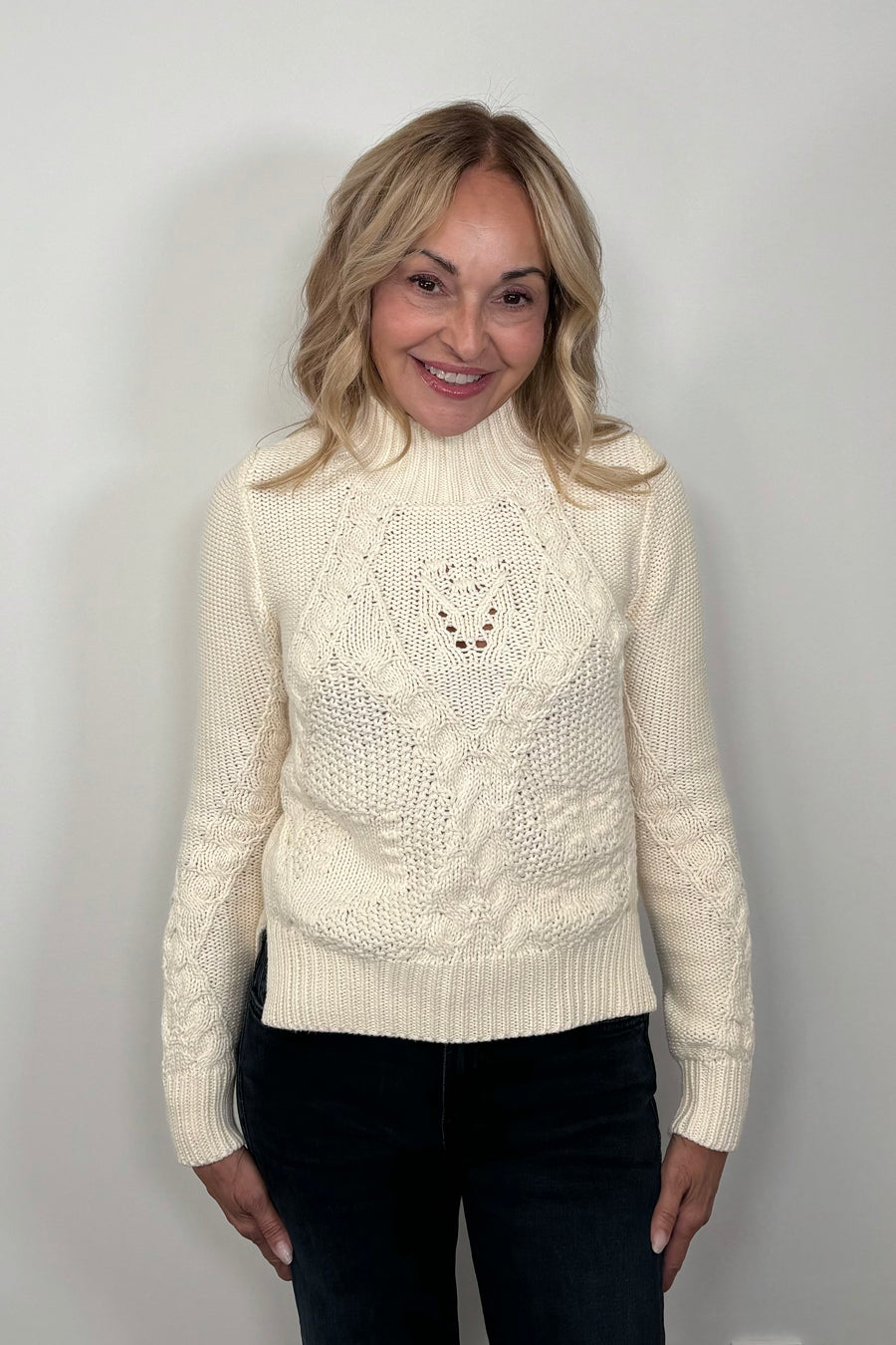 Front view of a woman wearing a cream-colored cable knit sweater 