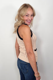 Woman wearing a beige knitted vest with black trim on a white background