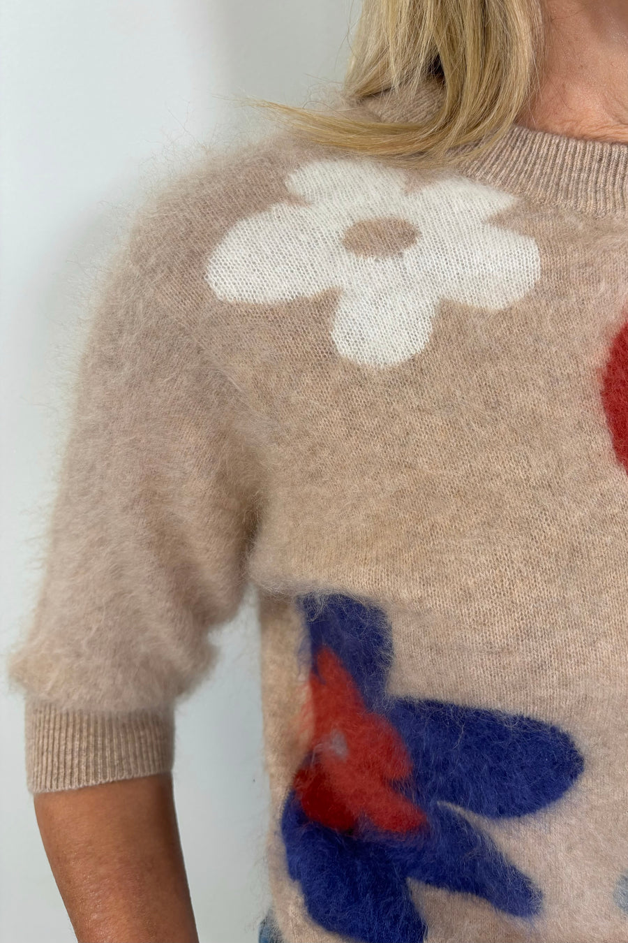 Zoom in of the right shoulder of a woman wearing a tan 100% brushed cashmere sweater with a flower pattern 