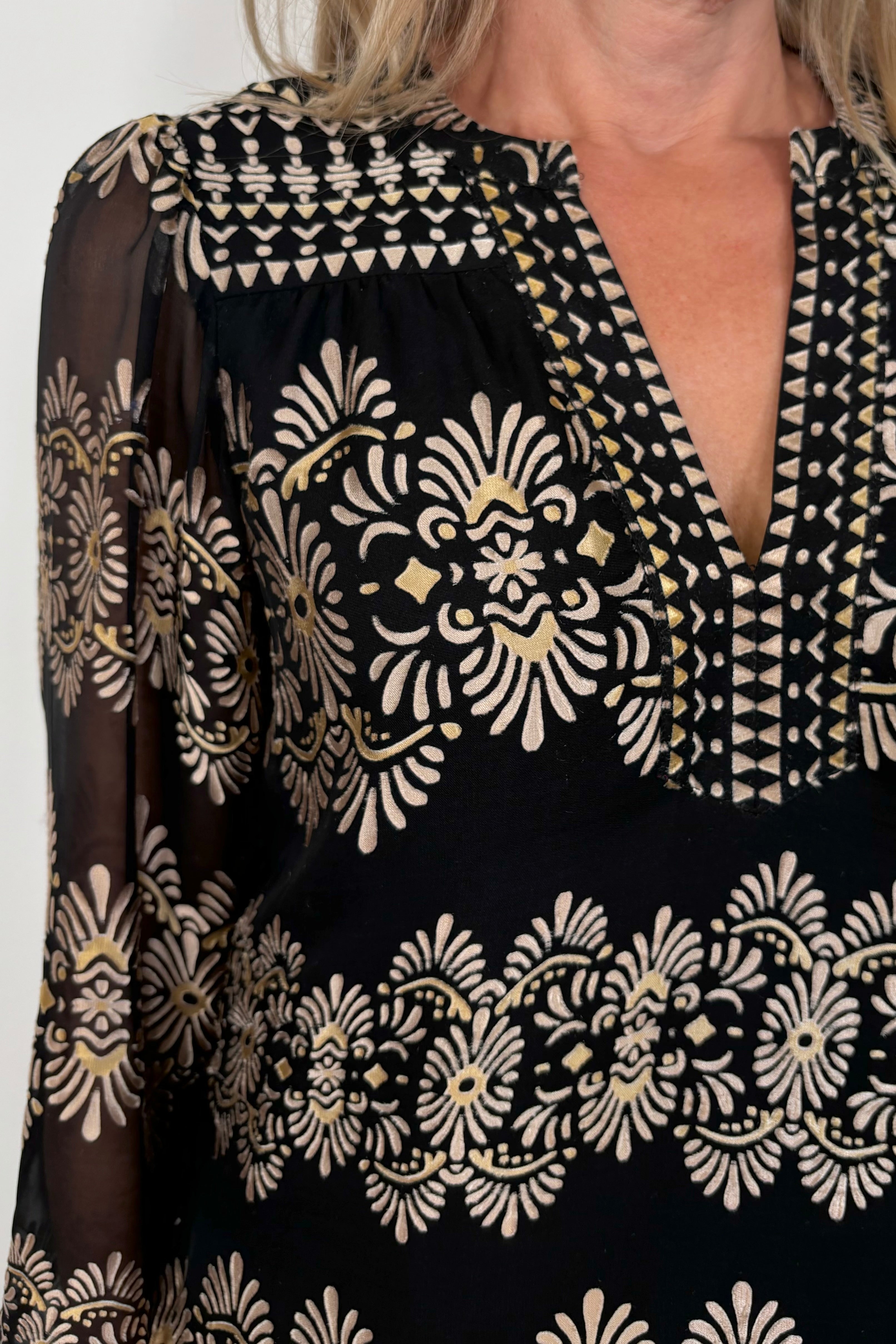 Close-up of woman wearing a silk mix black and gold long sleeve burnout blouse tucked in