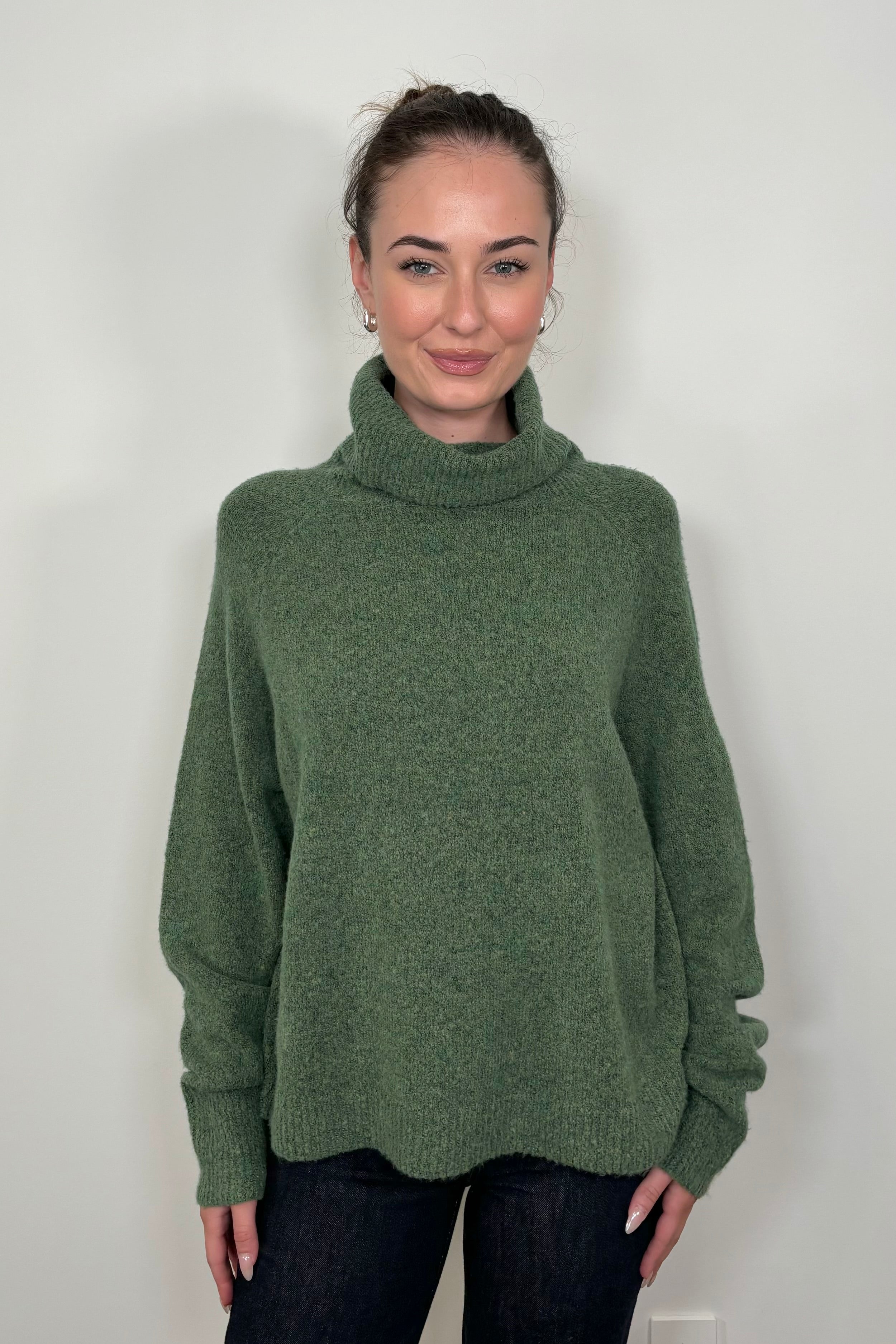 Front view of woman wearing an oversized green knitted turtleneck 
