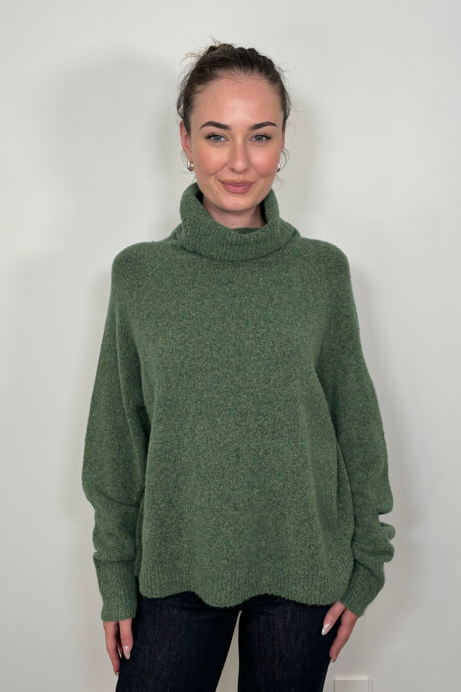 Front view of woman wearing an oversized green knitted turtleneck 